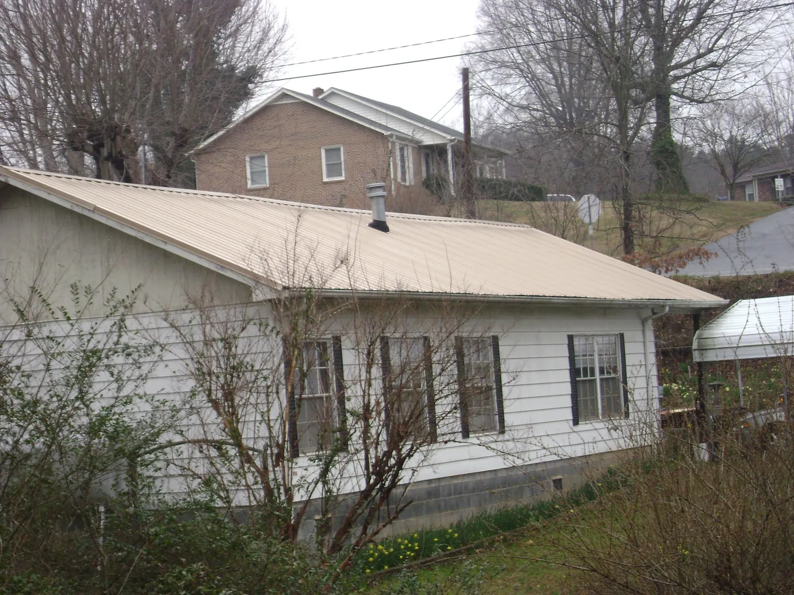 Tan metal roof on a white sided house set into a hillside — Commercial Roofing by Roofing Brothers in Bainbridge
